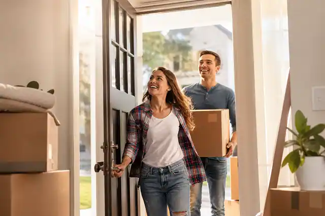 Happy first-time home buyers entering their new house with moving boxes using home buyer grants assistance